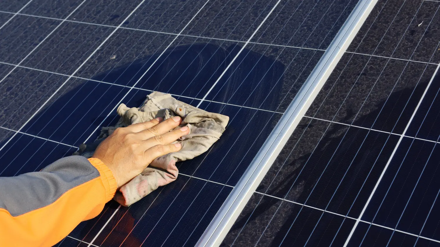 Die Hände einer Frau wischen mit einem Handtuch schmutzige und eklige Solarmodule mit Staub und Vogelkot im Freien ab, mit Kopierraum.