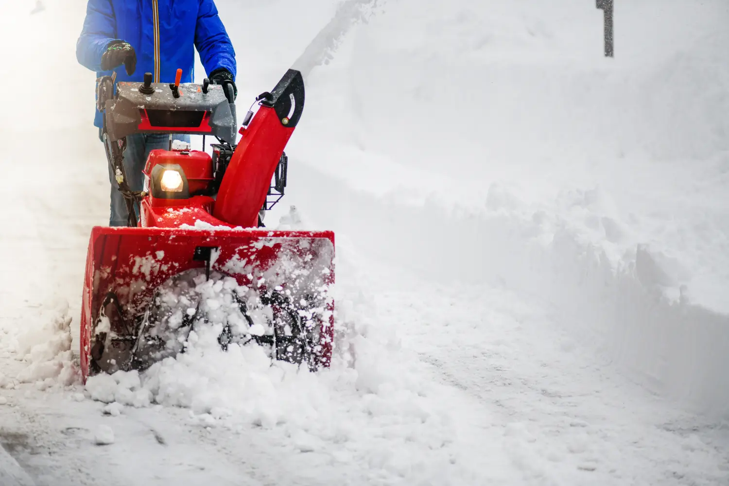 Mann räumt oder entfernt Schnee mit einer Schneefräse auf einer verschneiten Straße, Detail.